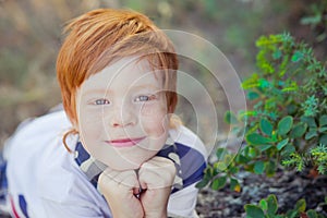 Cute red hair boy smiling to camera and standing in forest with horse