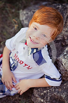 Cute red hair boy smiling to camera and standing in forest with horse