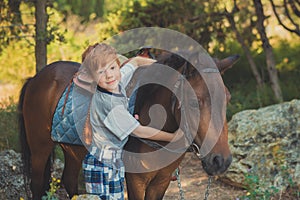 Cute red hair boy smiling to camera and standing in forest with horse