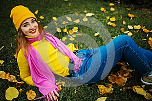 Cute red hair woman with teeth smile in yellow sweater holding autumn leaves in nature.