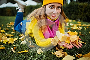 Cute red hair woman in yellow sweater holding autumn leaves in nature.