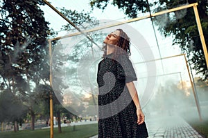 Cute red-haired curly girl rejoices under the water fogger in the city center