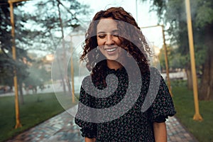 Cute red-haired curly girl rejoices under the water fogger in the city center