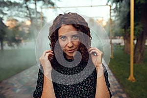 Cute red-haired curly girl rejoices under the water fogger in the city center