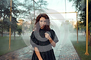 Cute red-haired curly girl rejoices under the water fogger in the city center