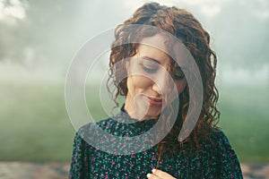 Cute red-haired curly girl rejoices under the water fogger in the city center