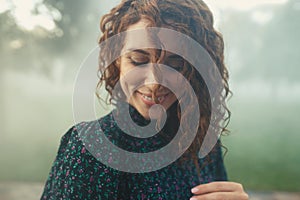 Cute red-haired curly girl rejoices under the water fogger in the city center