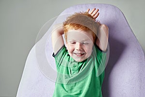 Cute red haired freckled little boy in green t-shirt waiting for doctor in medical office