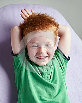 Cute red haired freckled little boy in green t-shirt waiting for doctor in medical office