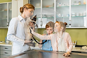 Cute red haired girl ausculting cat at clinic