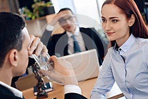 Cute red-haired woman looks at man, drinking glass of water in lawyer`s office for divorce.