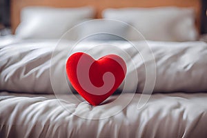 Cute red heart on a white bed, blurred background.