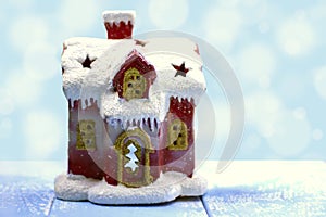 Cute red snow-covered house with windows on a light blue background with bokeh. Copy space