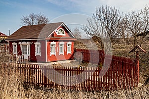 Cute red wooden house with white carved platbands surrounded by a wooden palisade in Rostov the Great.