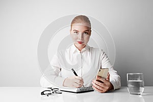 Cute redhead business woman working at the table over empty white background.