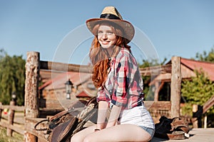 Cute redhead cowgirl sitting and resting on the ranch fence