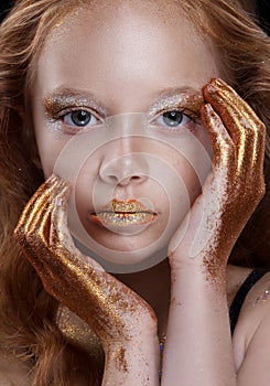 Cute redhead teenage model with bright makeup and colorful glitter and sparkles on her face and body.