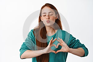 Cute redhead woman pucker lips, kissing and showing heart I love you sign, like you, feeling tender and romantic