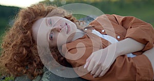 Cute redhead woman resting alone lying on the top of a cliff in mountain