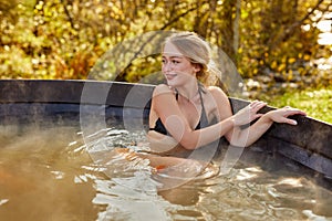 Cute relaxed caucasian woman sits inside of hot bath outdoors