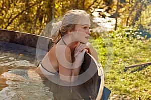 Cute relaxed caucasian woman sits inside of hot bath outdoors