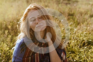 cute relaxed expression of the face with closed from the naked eyes of the girl sitting on the grass in the steppe with