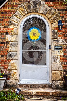 Cute rock framed door in brick house with arched storm door and blue and yellow wreath in support of Ukraine photo