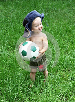 Cute Russian toddler boy in a ushanka hat is holding a soccer or football ball in his hands. Russian football fun concept photo