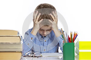 Cute sad schoolboy sitting at the table with books and notebooks. Tired of doing homework. Isolated on a white background.