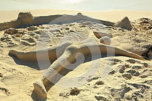 Cute sand sculpture representing a human laying on the beach with face down. Aruba island. Caribbean.