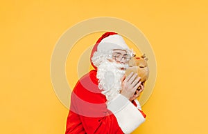 Cute Santa Claus hugging a toy deer on a yellow background. Christmas and New Year concept. Santa and a plush toy