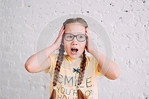Cute scared tweens girl in glasses with long hair  on white brick wall