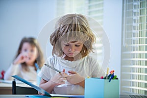 Cute school boy drawing in classroom. Pretty stylish schoolkid studying homework math during lesson at classroom