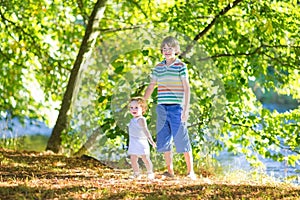 Cute school boy holding his baby sister at river shore