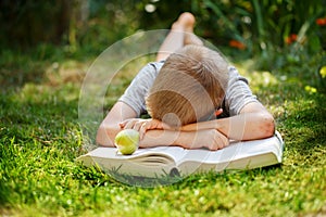 Cute school boy lying on a green grass who does not want to read the book. boy sleeping near books