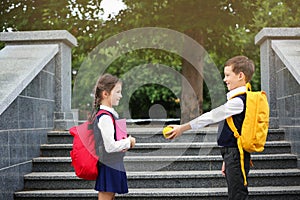 Cute school boy offering apple to girl with stationery