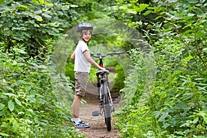 Cute school boy riding a bike in summer park