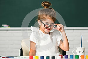 Cute school girl face with glasses. Little girls drawing a colorful pictures with pencil crayons in school classroom