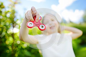 Cute school girl playing with fidget spinner on the playground. Popular stress-relieving toy for school kids and adults.