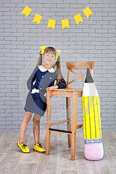 Cute school girl posing in studio shoot in school uniform dress and jacket on background of letters or grey brick wall. Teen