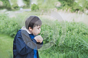 Cute School kid blowing dandelion flower in spring park while walking to school in the morning. Happy child boy having fun