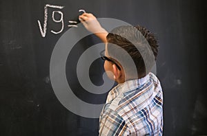 Cute schoolboy boy solves a math problem on a black blackboard