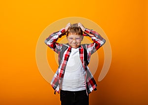 A cute schoolboy in a plaid shirt holds his head with his hands. isolation on a yellow background