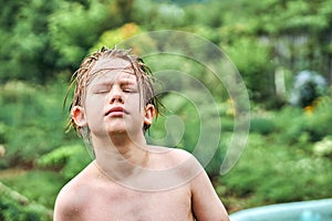 Cute schooler with wet blond hair stands against lush trees