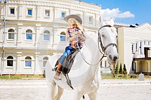 Cute schoolgirl fond of equestrianism riding horse on weekend