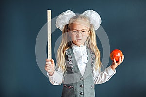 Cute schoolgirl with glasses and red Apple in hand looking like a strict teacher raised her pointer to draw attention. Educational