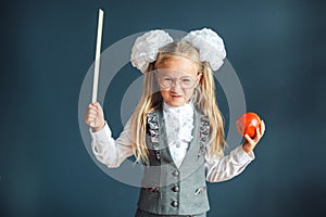 Cute schoolgirl with glasses and red Apple in hand looking like a strict teacher raised her pointer to draw attention. Educational