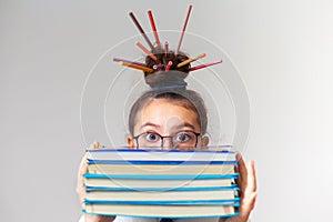 Cute schoolgirl on a gray background. Looks from behind a stack of books with a puzzled look. looks scared