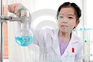 Cute schoolgirl in lab coat doing simple science experiments, Asian child scientist pouring blue chemical into bottle flask.