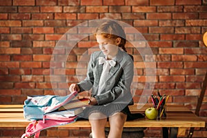 Cute schoolgirl puts textbook into the schoolbag